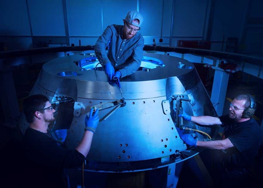 three male employees work on the orion spacecraft